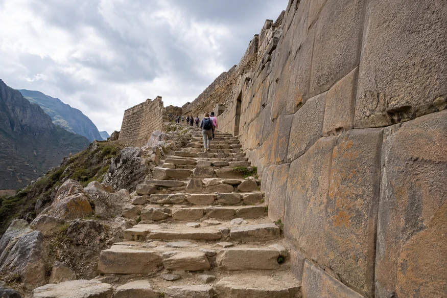 Visitors climbing original stone steps beside fitted Inca walls at Ollantaytambo ruins