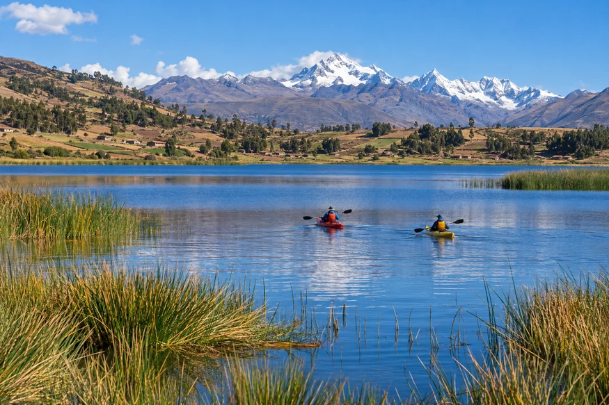 Kayakers on Huaypo Lagoon with Andean farmland and mountains near Cusco Peru